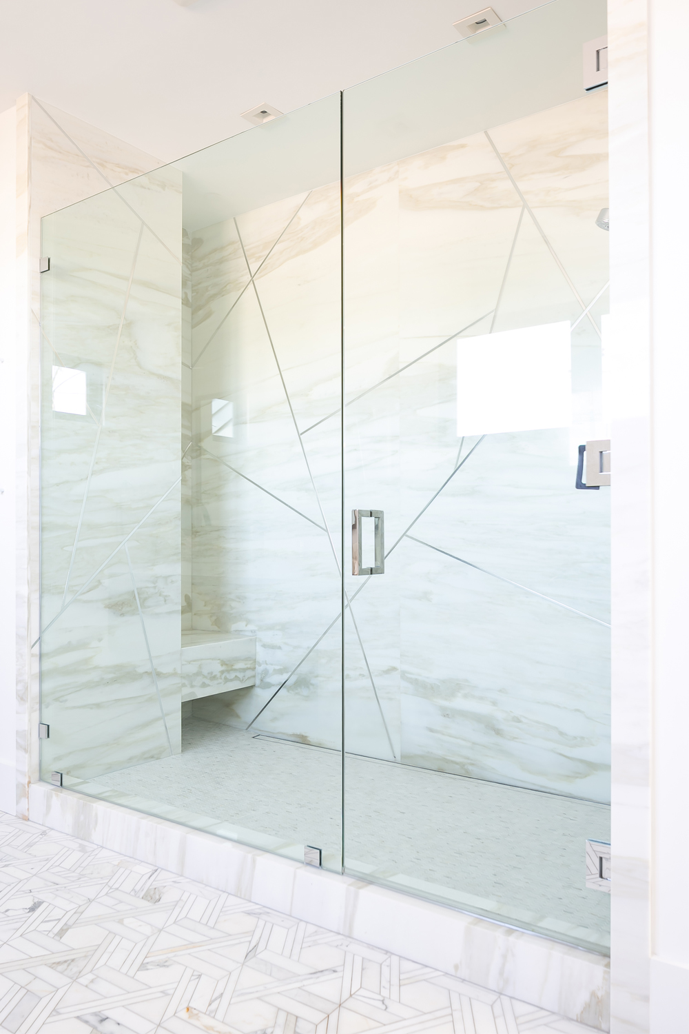 A modern glass shower enclosure with marble walls and floor, featuring sleek diagonal lines and a built-in bench inside the shower.