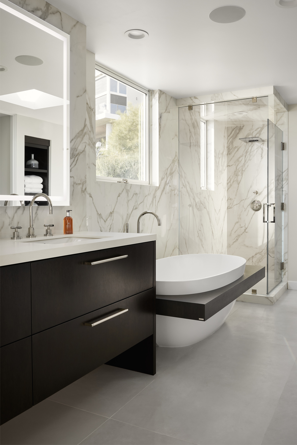 A contemporary bathroom with marble walls, a floating bathtub, dark wood vanity with chrome fixtures, and a glass shower enclosure.