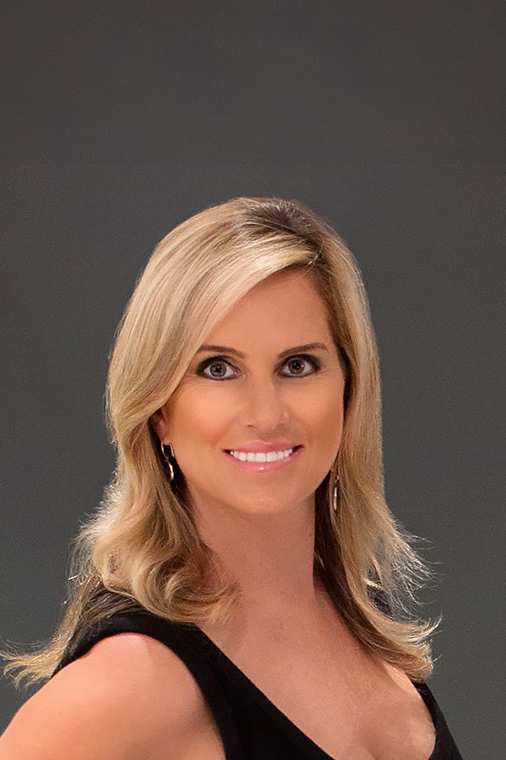 A headshot of a woman with blonde hair, smiling, wearing a black top and earrings, set against a dark background.