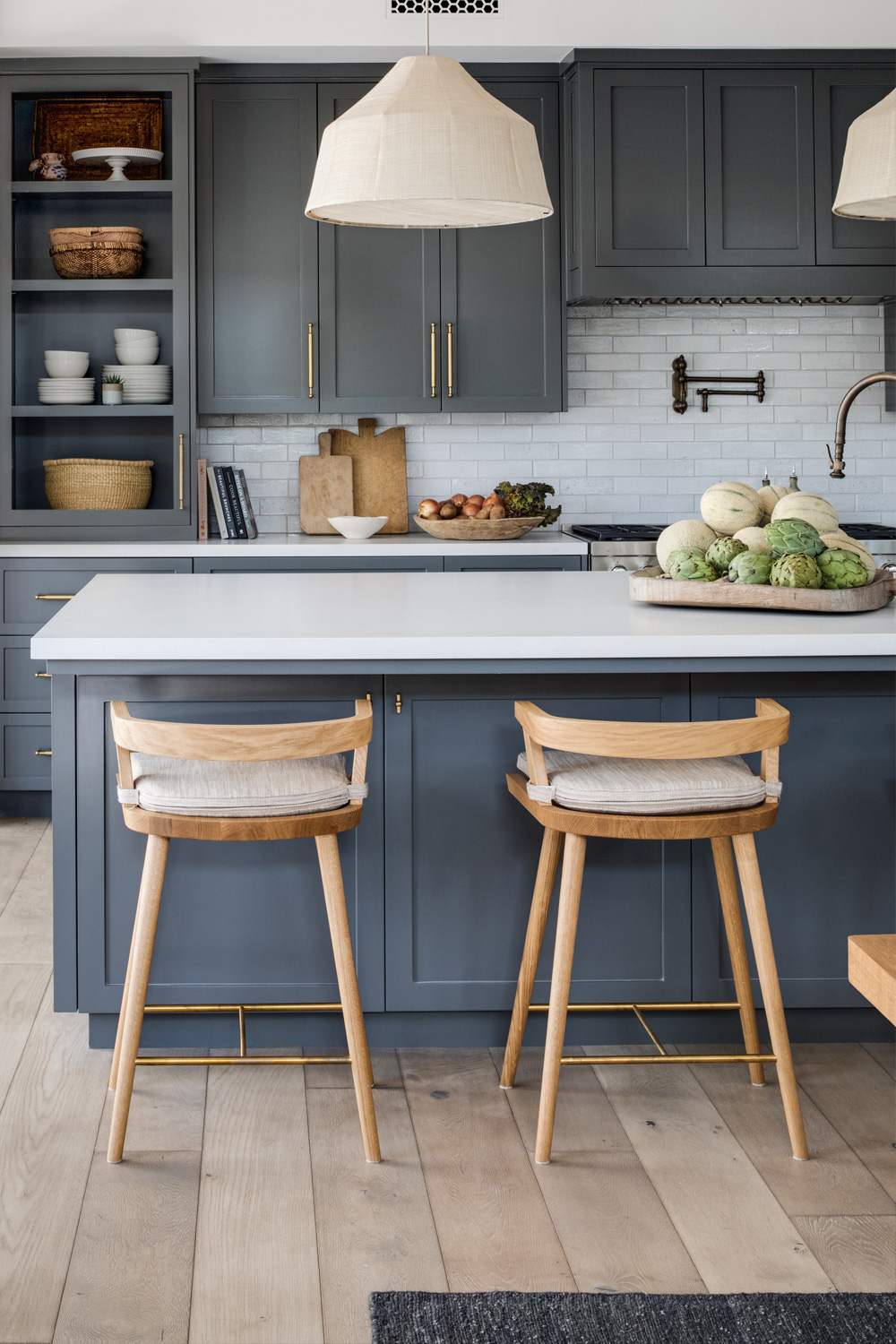 A stylish kitchen with dark gray cabinets, a white island countertop, wooden stools with cushions, and pendant lights above the island.