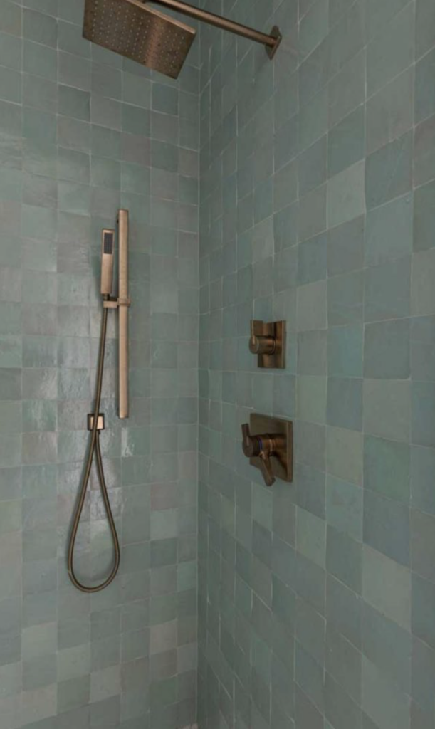 Luxury primary shower featuring handcrafted green wall tile and brass fixtures.