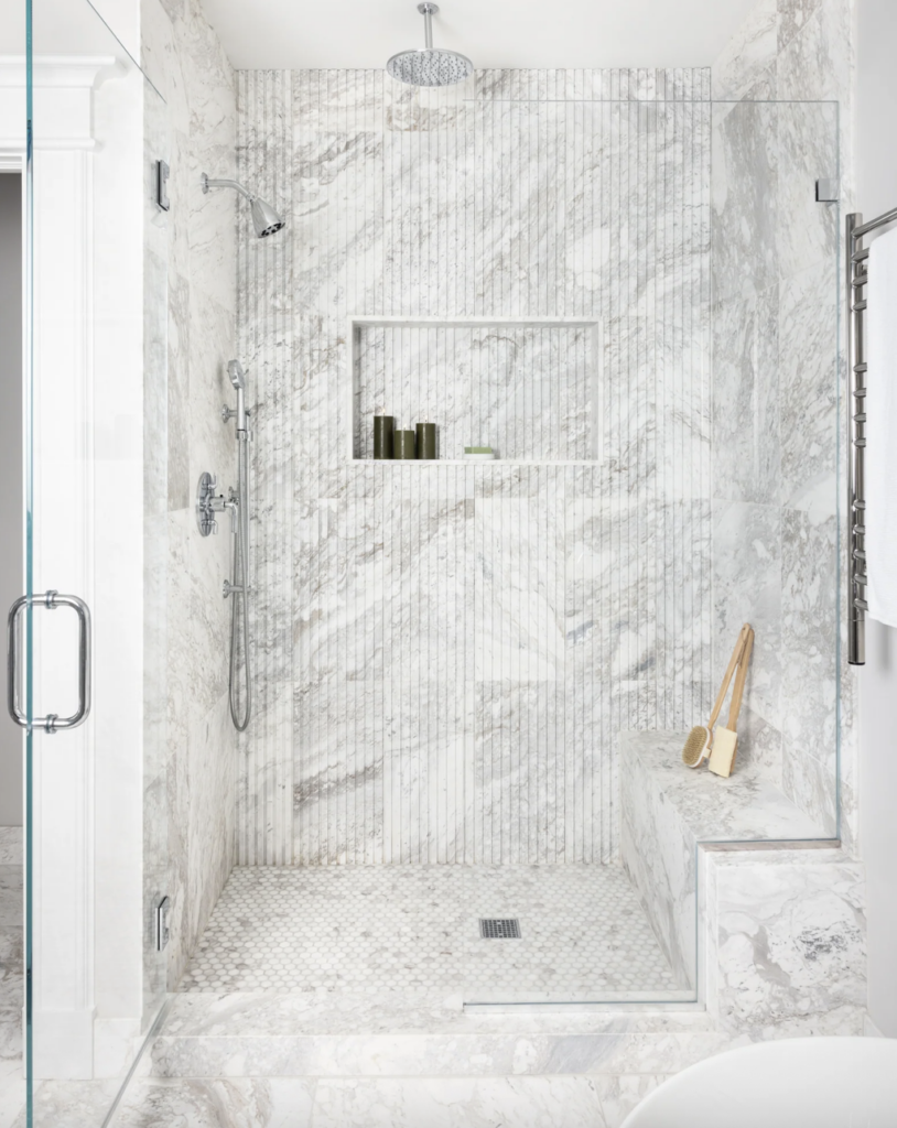 Luxury primary bathroom with a natural stone shower, frameless glass enclosure, and large-format wall tile in an Orange County home.